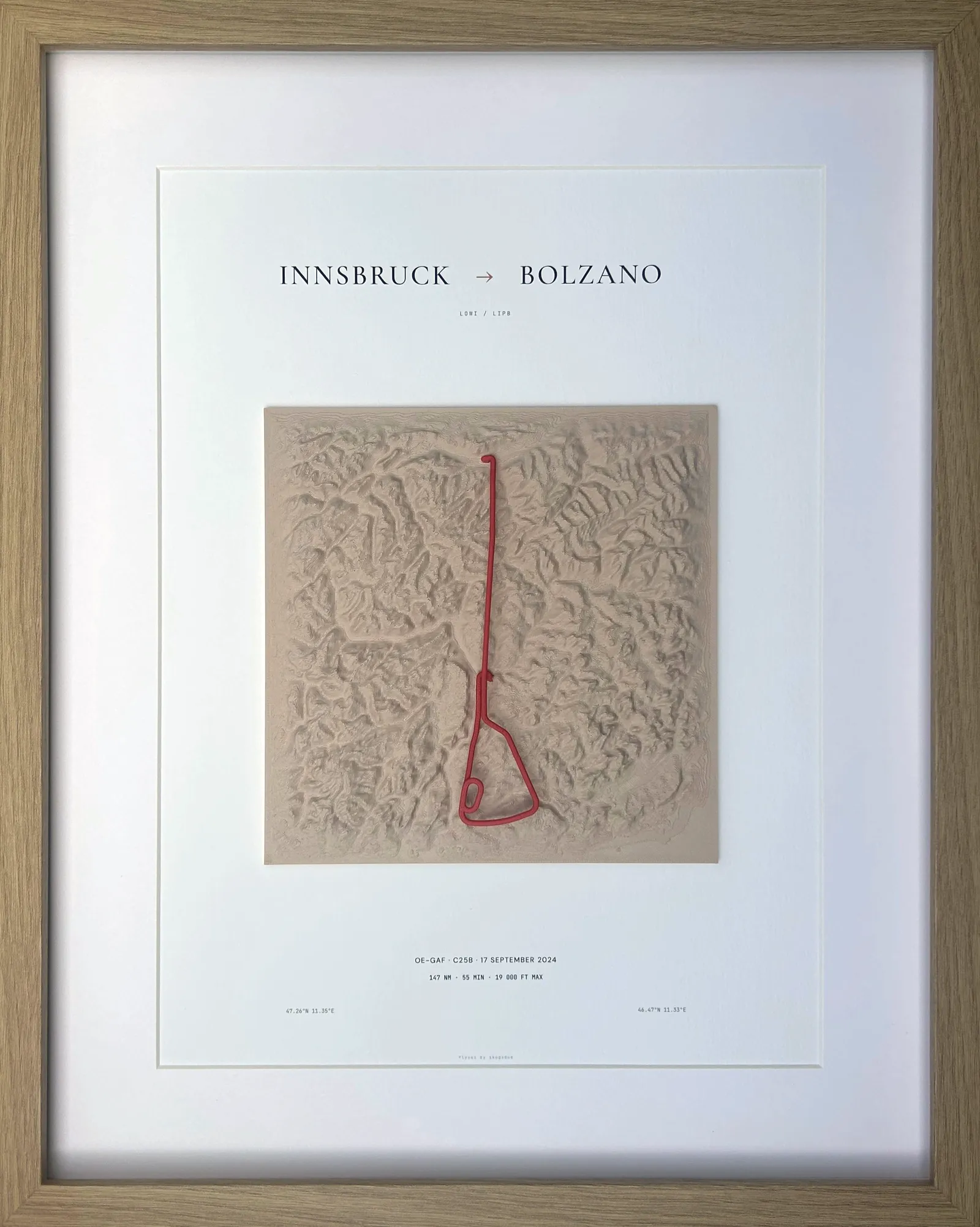 The framed flyvei piece, straight on: matte Sand terrain with the route from Innsbruck to Bolzano raised in Red, flight data on the poster beneath.
